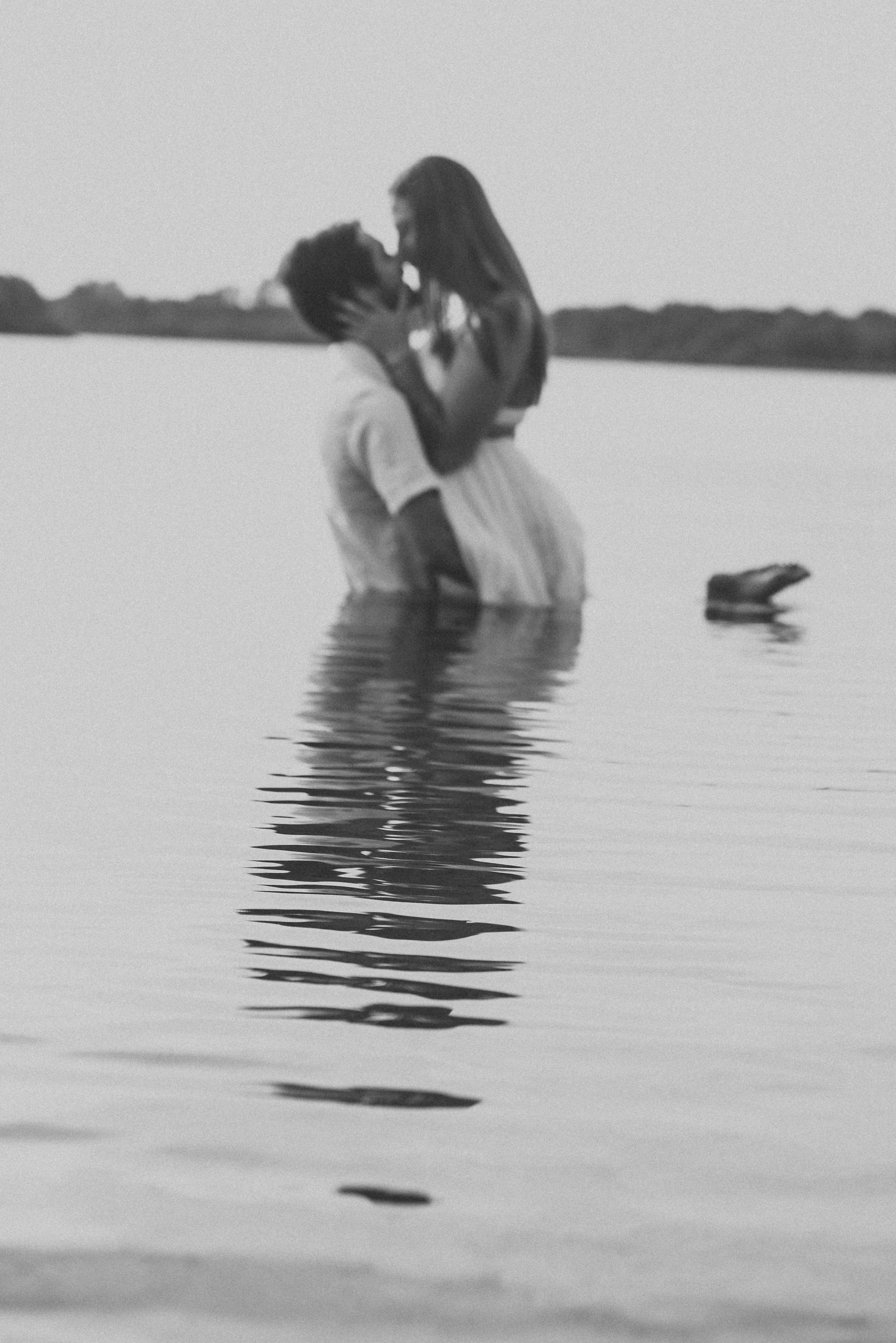 Artistic black and white photograph of figures partially submerged in still water.