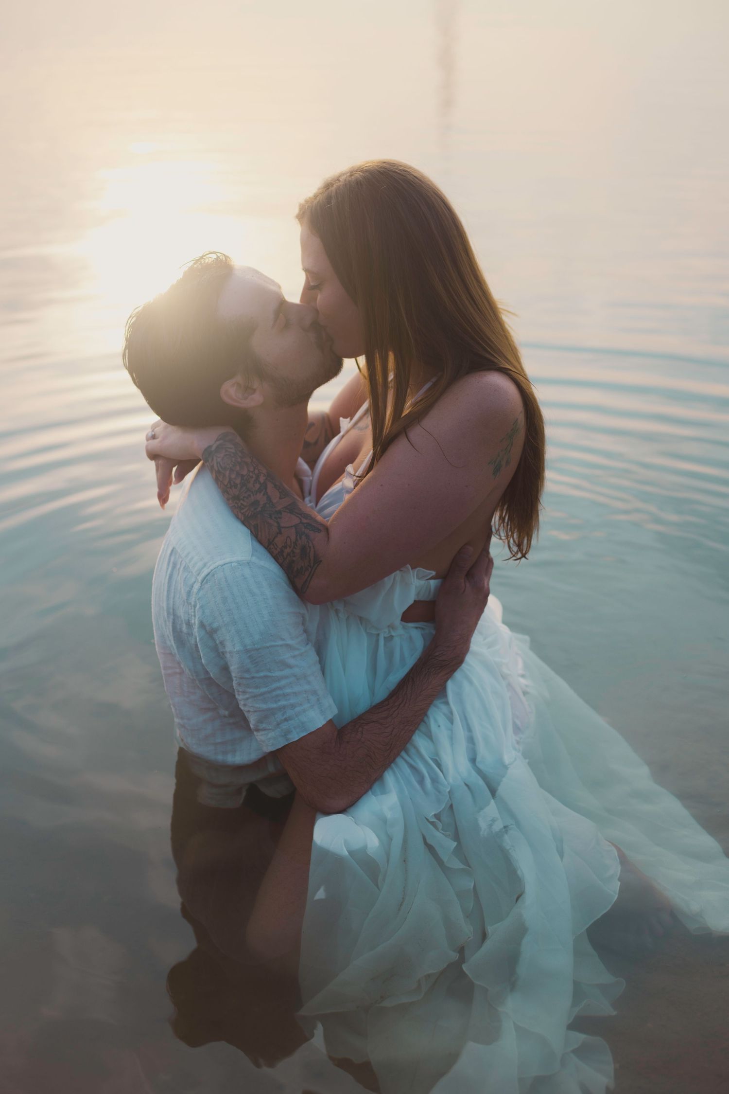 Couple shares intimate moments while standing in shallow water during golden hour.