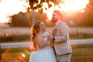 A couple shares a joyful moment during their outdoor wedding ceremony at sunset with golden light streaming through.