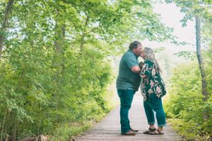 Couple in matching green outfits shares tender moments along a tree-lined path.