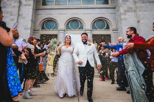Wedding guests throw confetti at a newly married couple outside a stone church building.
