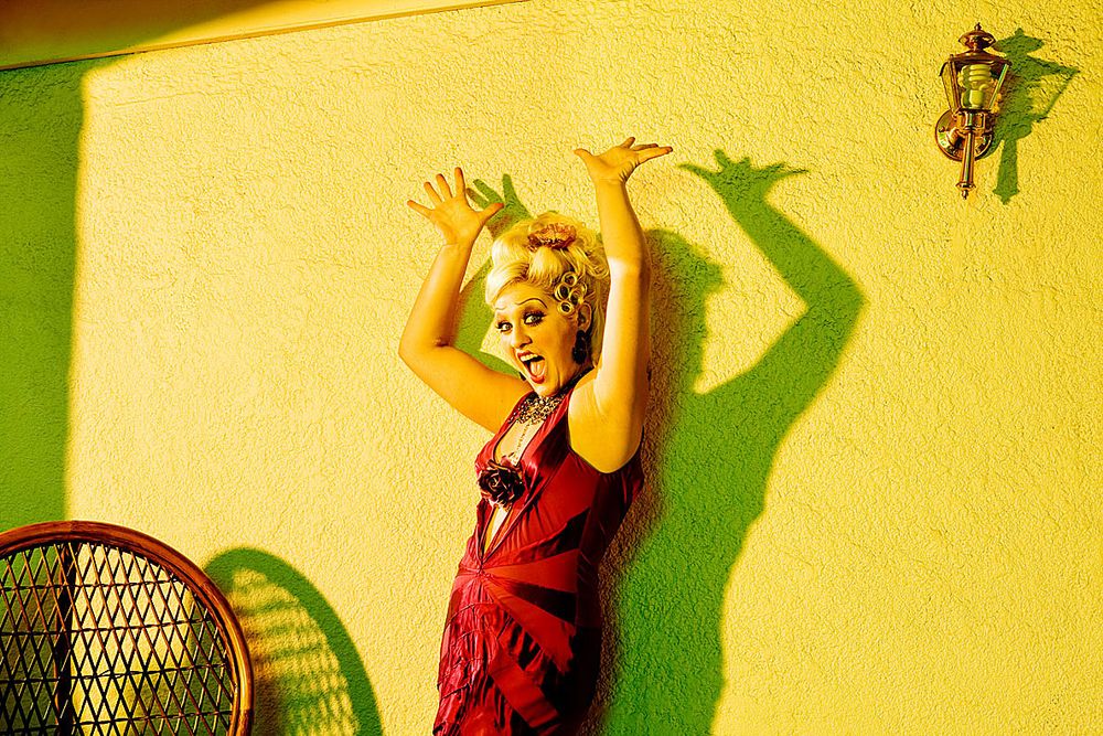 A person in a red dress poses against a yellow wall casting dramatic shadows in a dynamic fashion series.