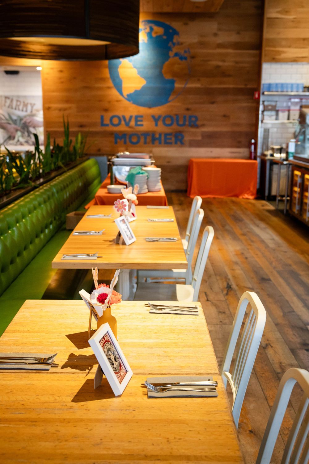 Modern restaurant interior with wooden tables, green banquette seating, and 'Love Your Mother' text on wooden wall.
