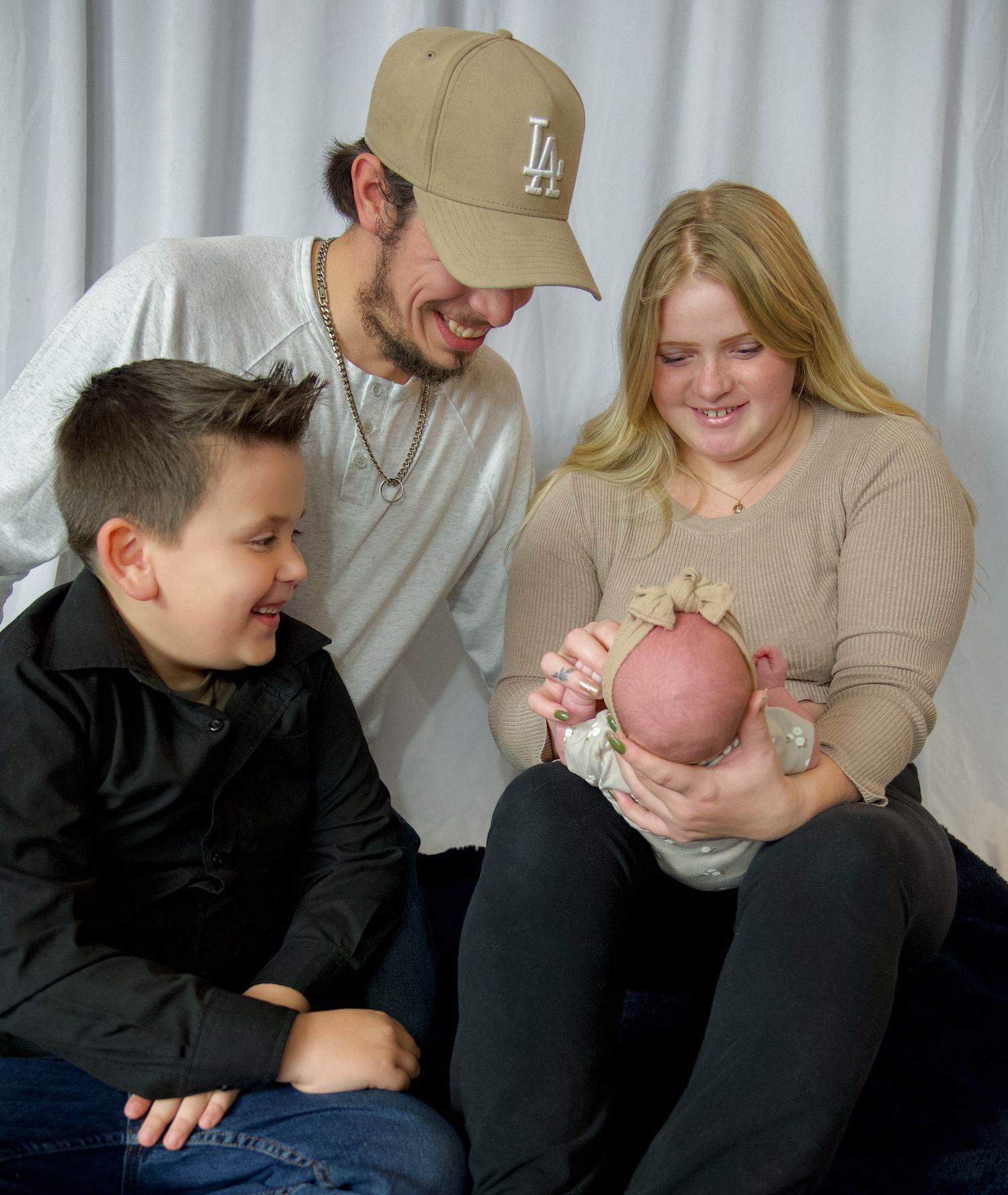 Happy family of four admiring their newborn baby together in a warm studio portrait session.