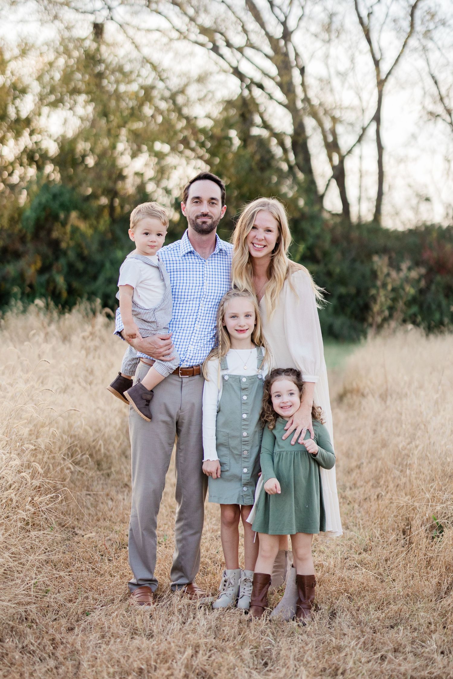A group poses together outdoors in a golden field during autumn wearing coordinated neutral-colored outfits.