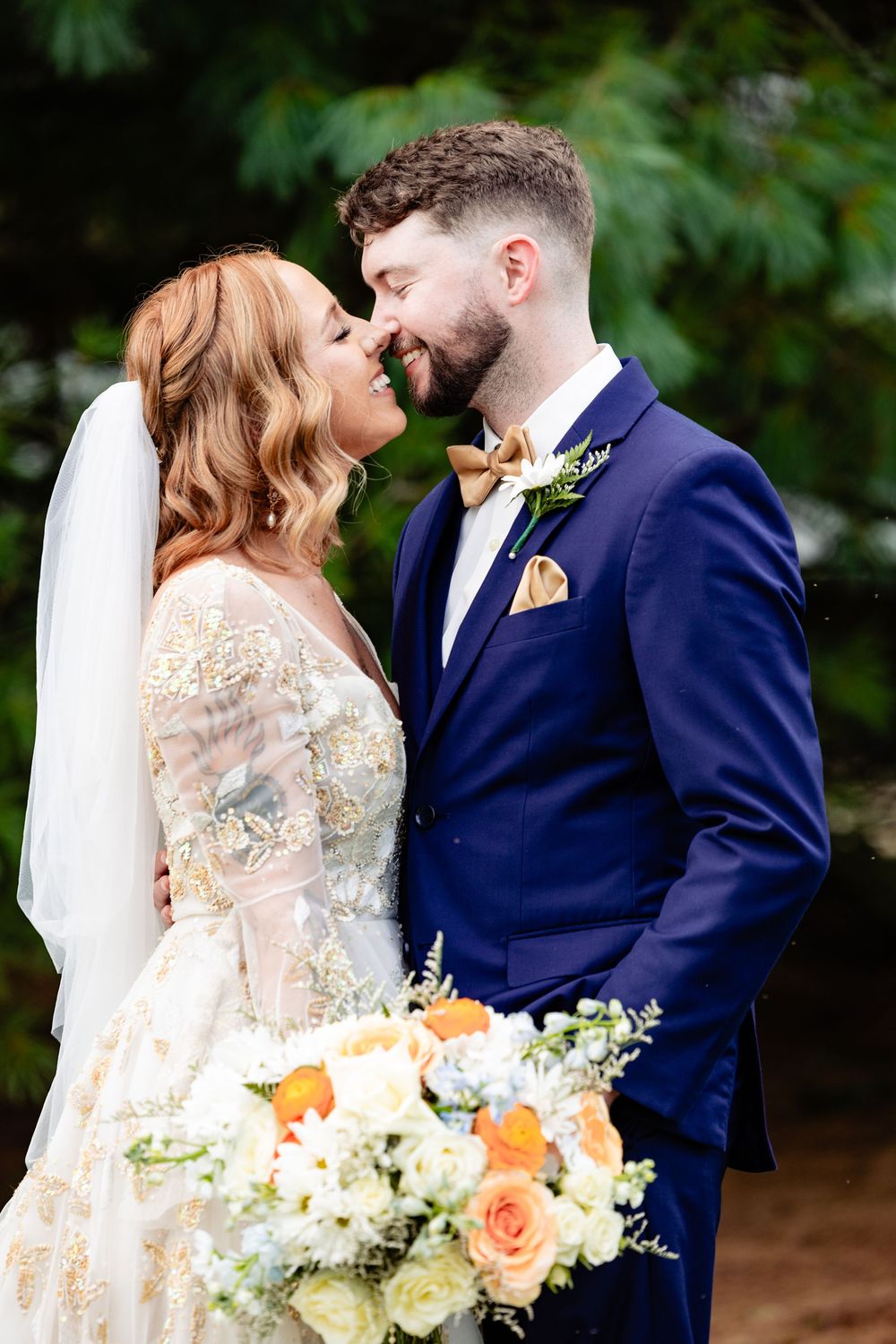Bride in gold embroidered gown and groom in navy suit share a romantic outdoor moment.