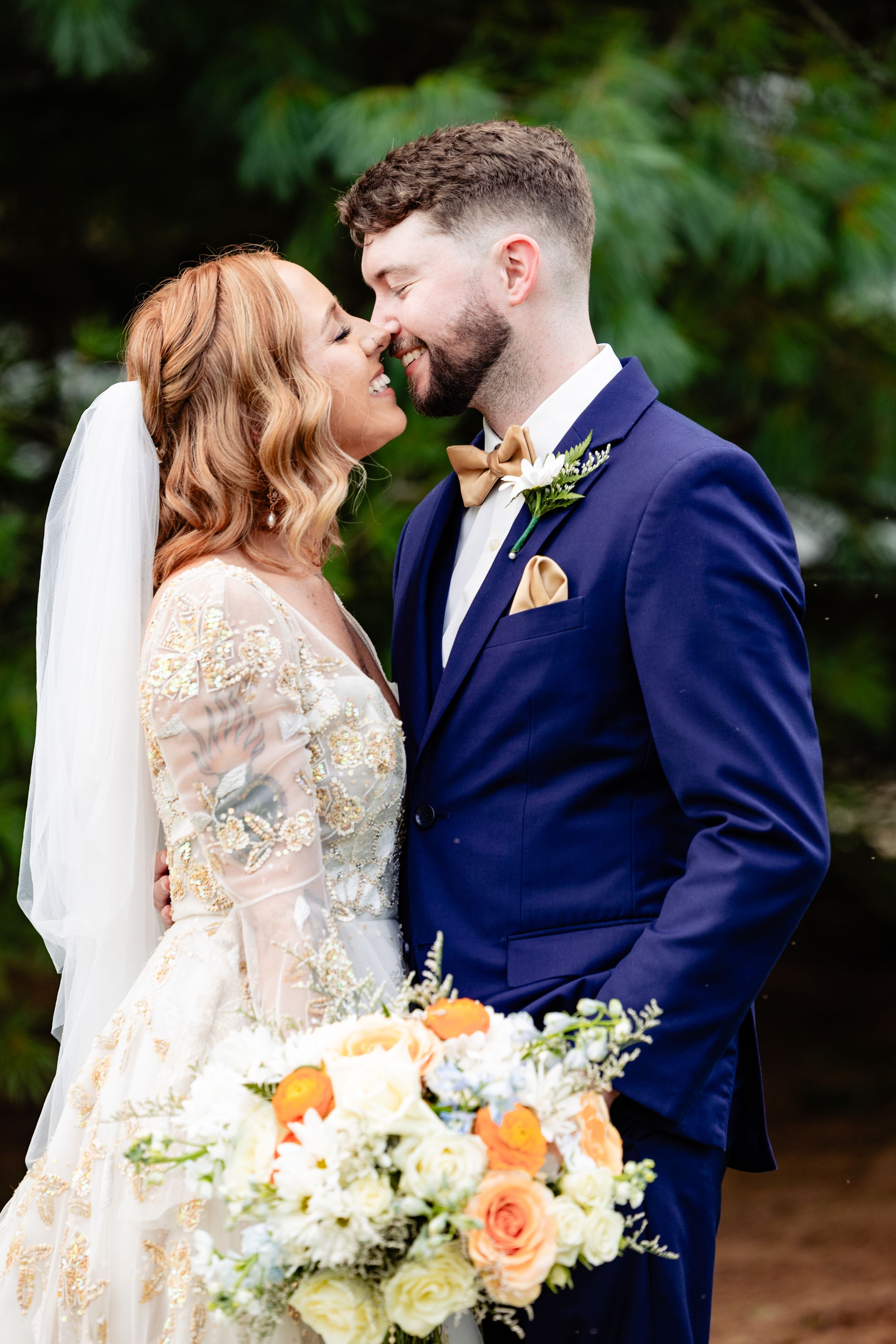 Bride in gold embroidered gown and groom in navy suit share a romantic outdoor moment.