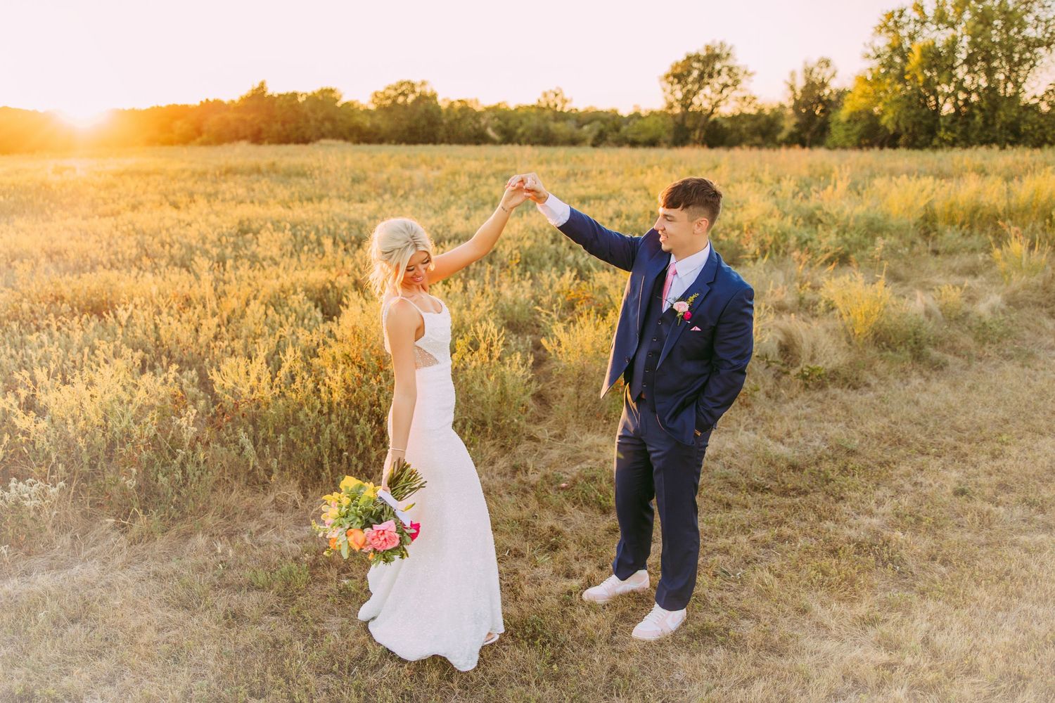 Newlyweds dancing in golden field during sunset.