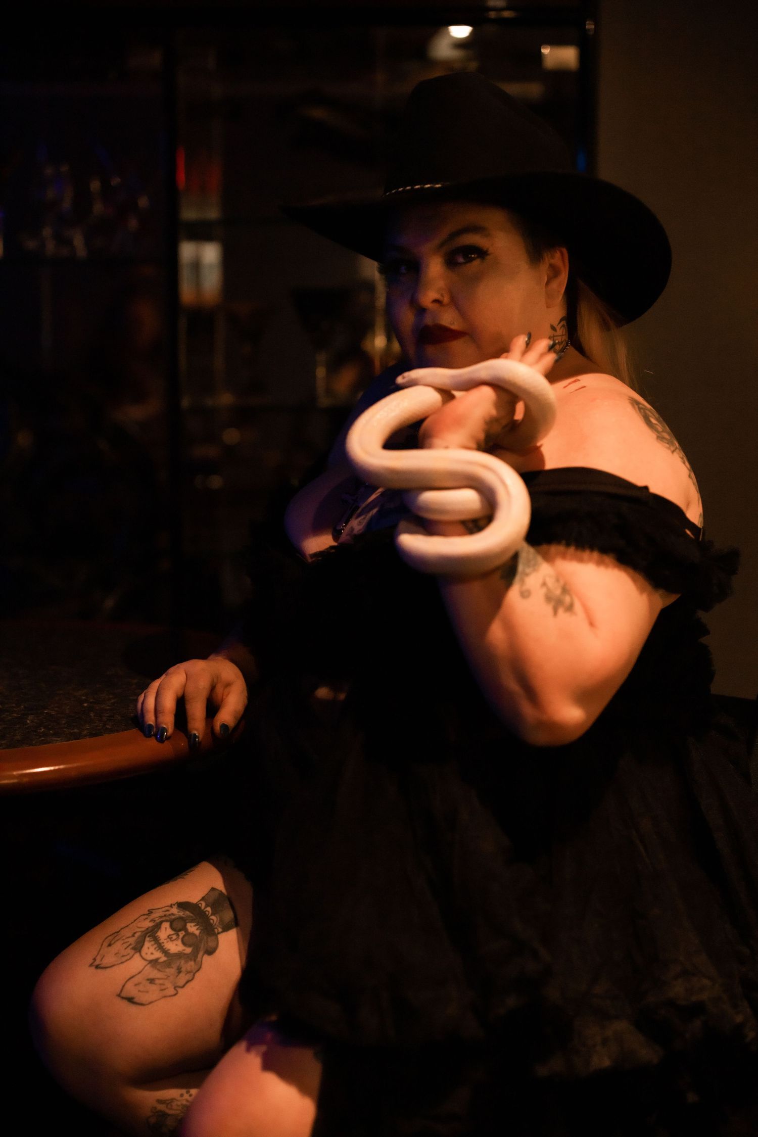 A woman in a black outfit and a black cowboy hat posing with a white snake
