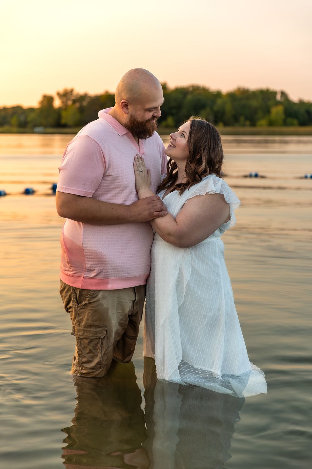 Couple shares intimate moments standing in shallow water during golden hour sunset photo session.