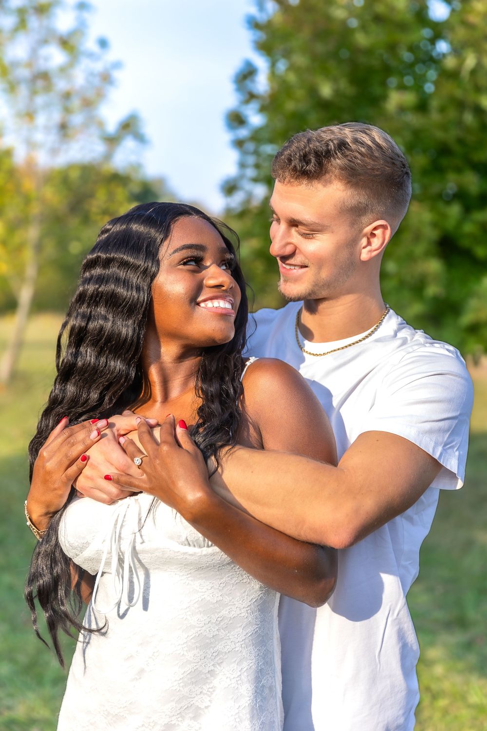 A couple shares an intimate moment while embracing outdoors against autumn trees.