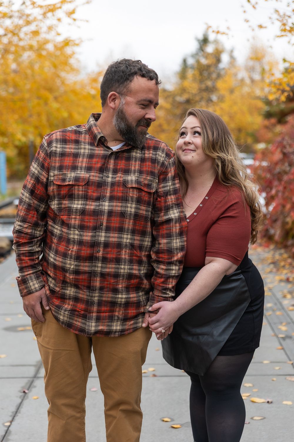 A couple shares joyful moments together during an autumn photoshoot with golden leaves in the background.