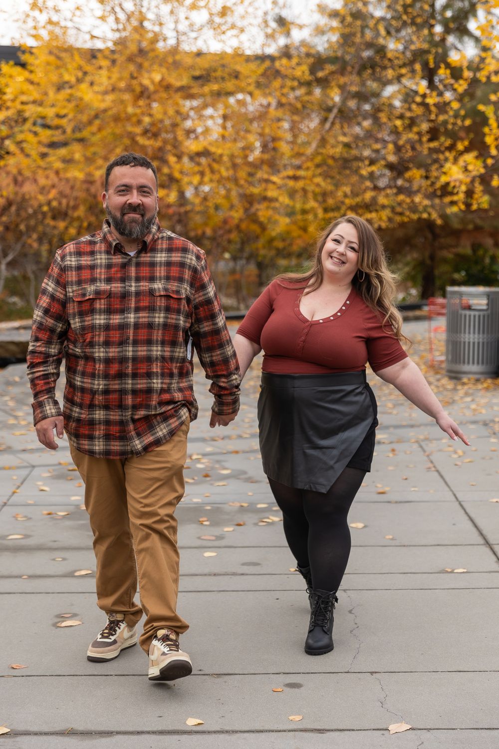 A couple walks hand in hand on a stone path surrounded by autumn trees with golden yellow foliage.