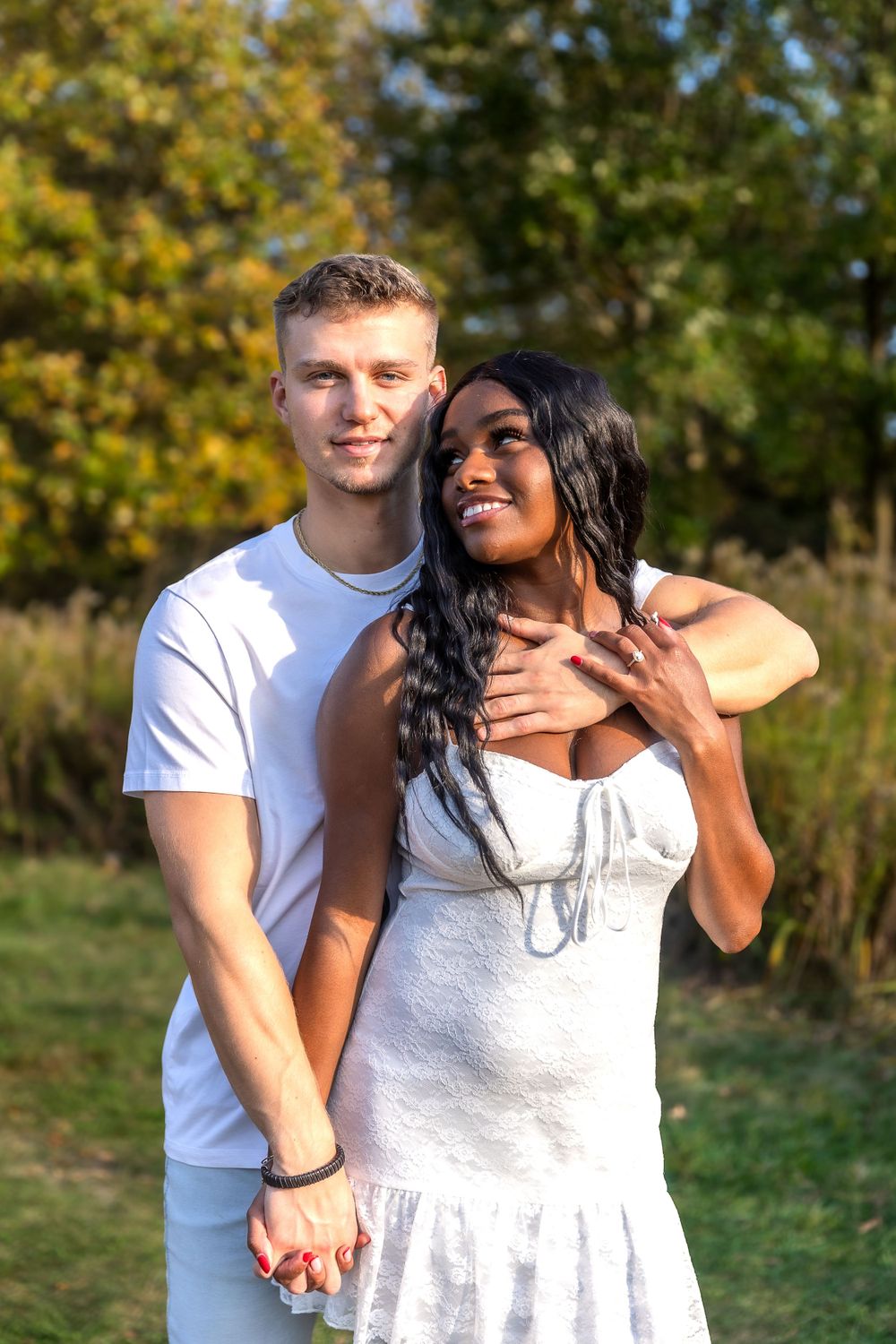 A romantic couple holds hands and poses together in a sunny autumn field.