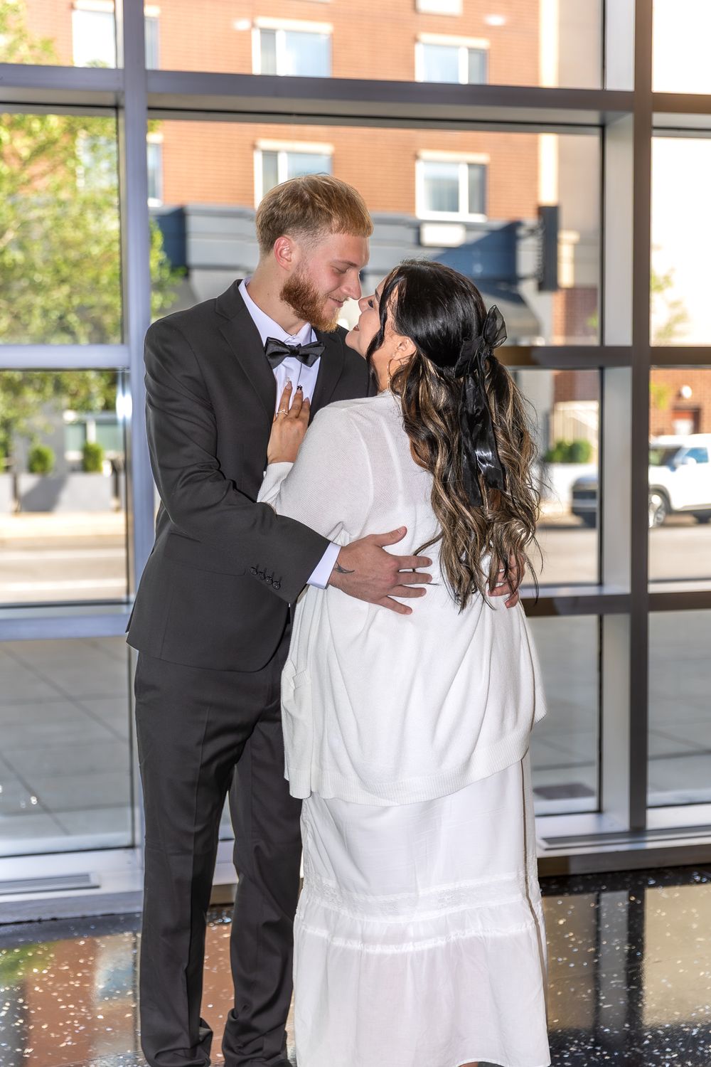 A couple in formal attire share a romantic kiss sequence at an indoor location with glass windows and brick walls.