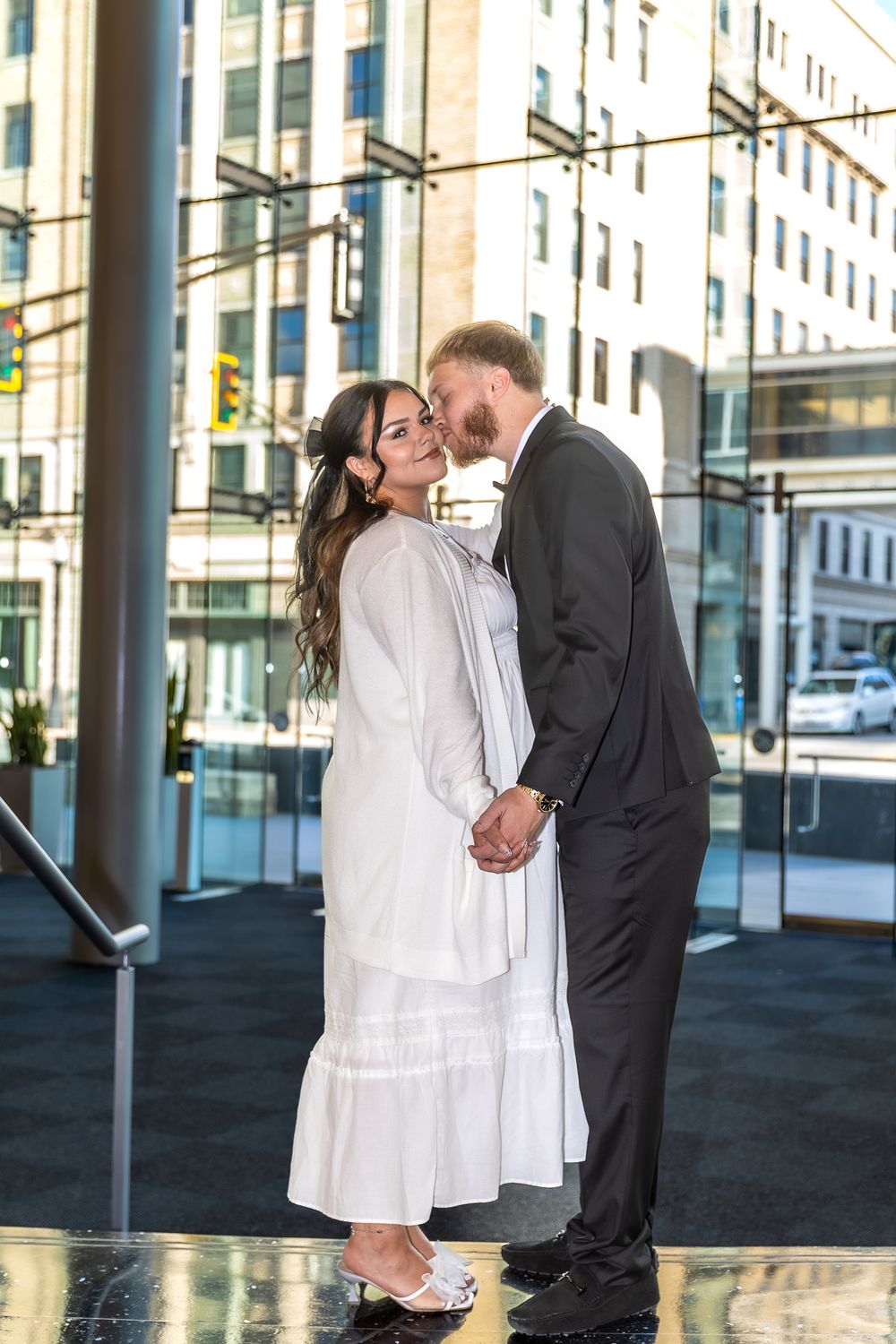 A romantic wedding photo series showing a couple embracing and kissing outdoors against an urban backdrop.