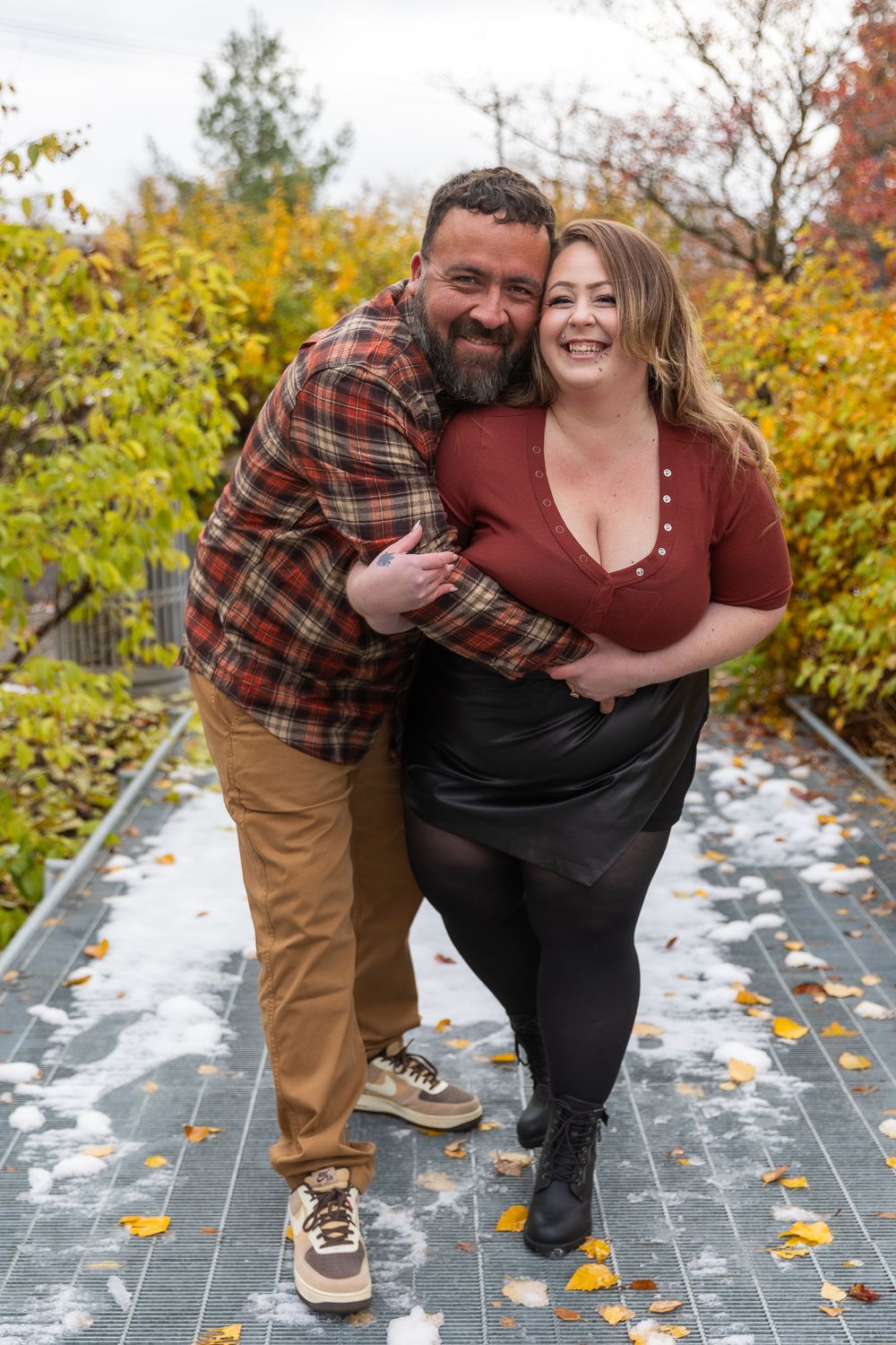 A couple shares a playful moment on outdoor steps surrounded by autumn foliage and fallen leaves.