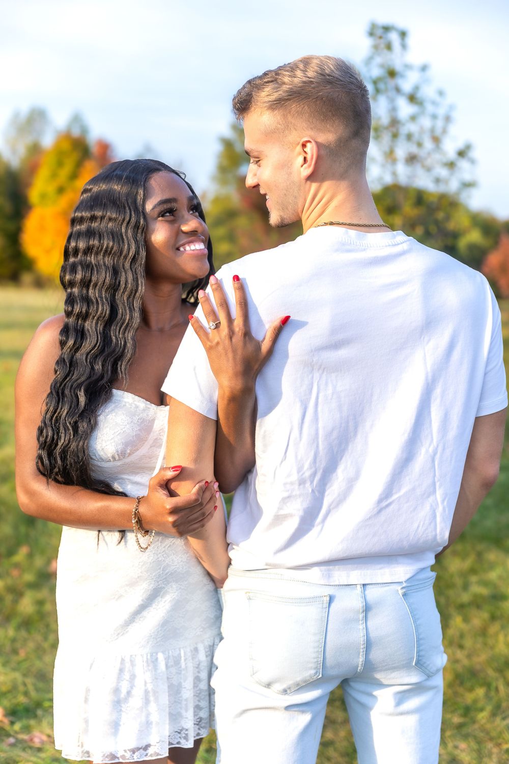 A couple in matching white outfits shares a tender moment in a sunlit autumn setting.
