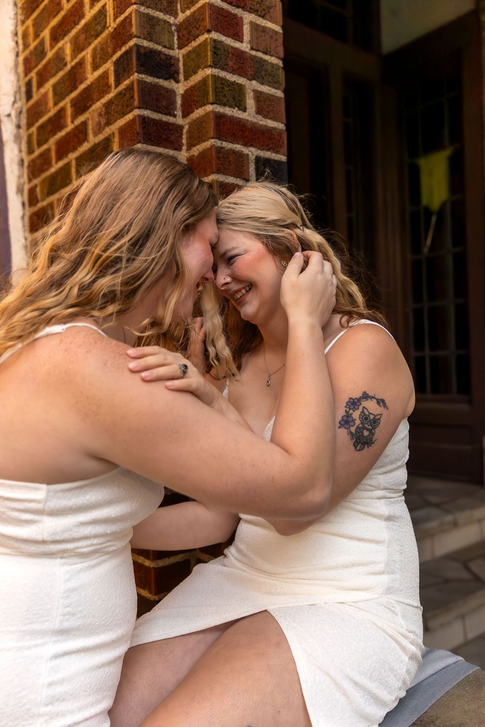 Intimate moment shared between two people in white dresses against a brick wall.