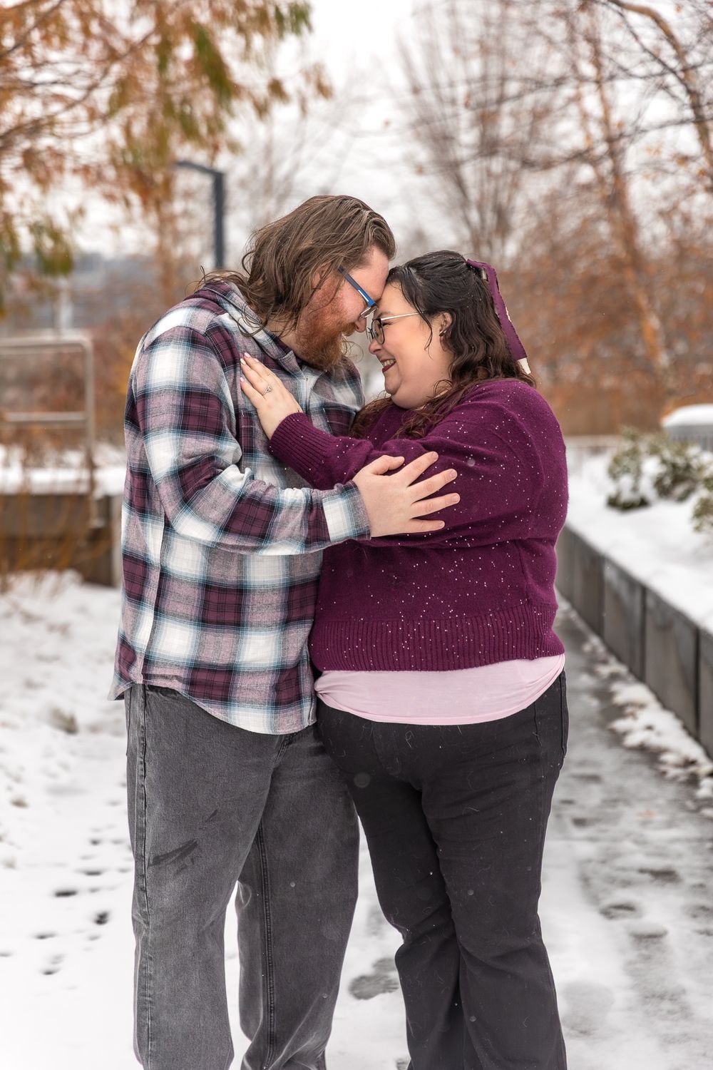 A couple shares an intimate moment together in a snowy winter setting while wearing casual plaid and purple attire.