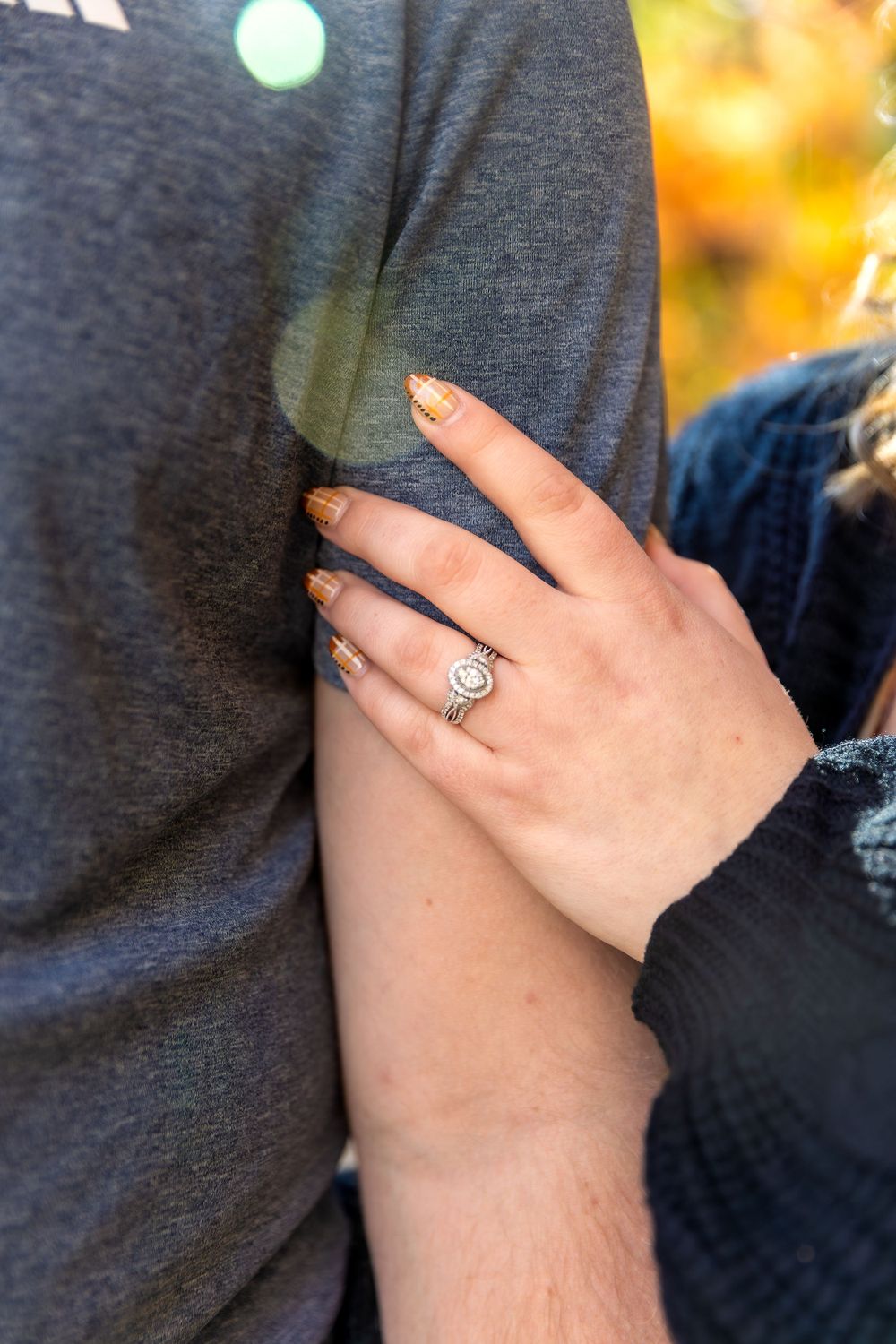 A close-up of an engagement ring on a hand resting against a gray shirt.