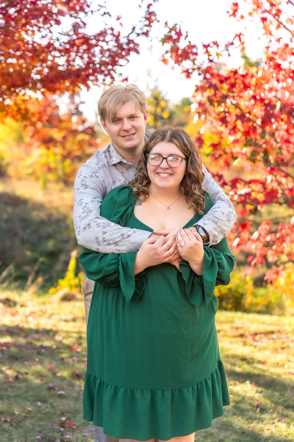 A couple embraces in front of vibrant red maple leaves during autumn.