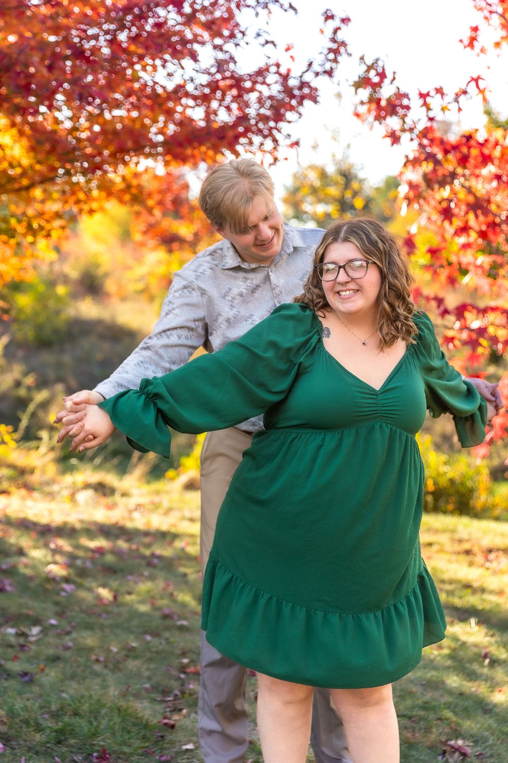 A joyful couple poses playfully in front of red autumn leaves.