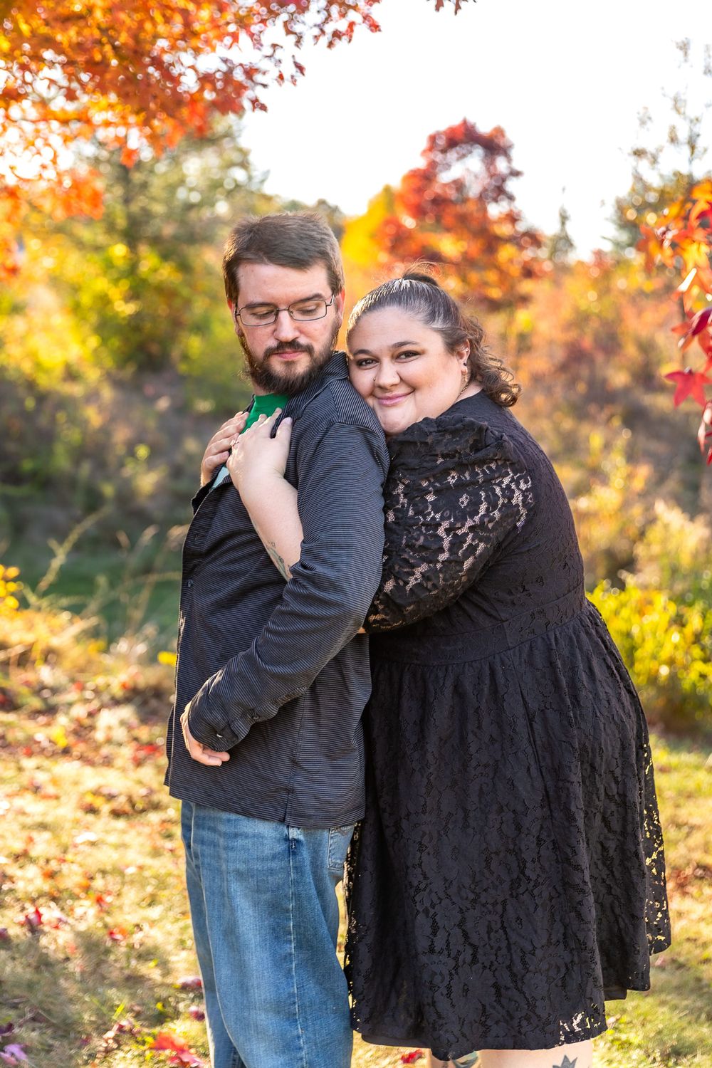 A couple embraces while standing among colorful fall trees with golden leaves.