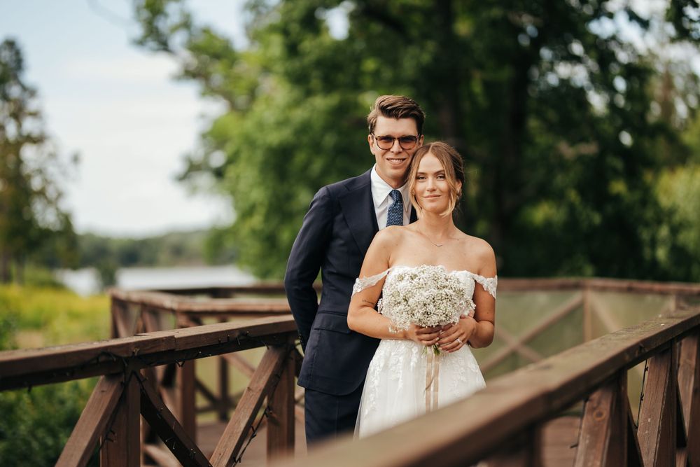 A couple stands on a rustic wooden bridge surrounded by greenery on their wedding day.