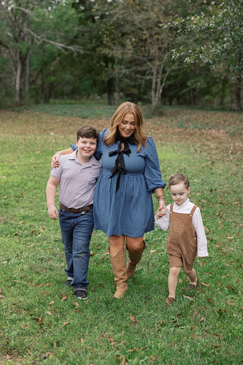 Three people walk together on grass with autumn trees in background wearing casual fall outfits.