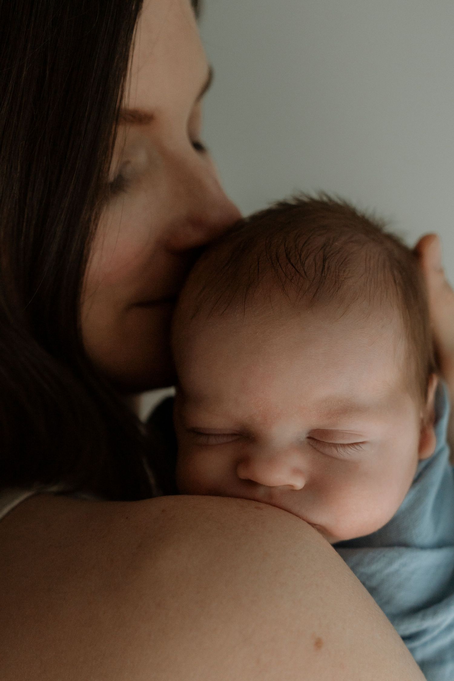 A tender intimate moment showing a baby sleeping peacefully against their parent's shoulder in a blue shirt.