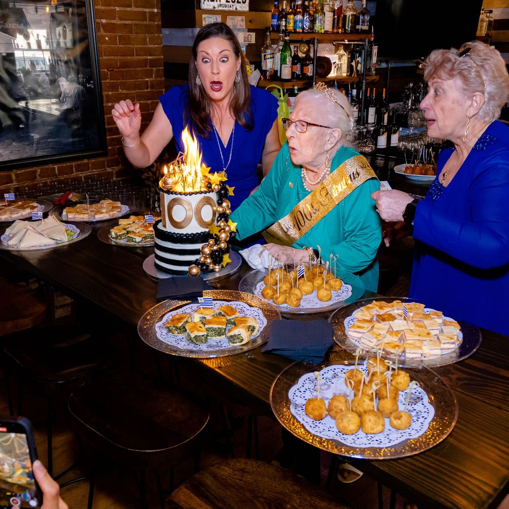 Birthday celebration at restaurant with surprised reaction to flaming cake and plates of food on wooden table.