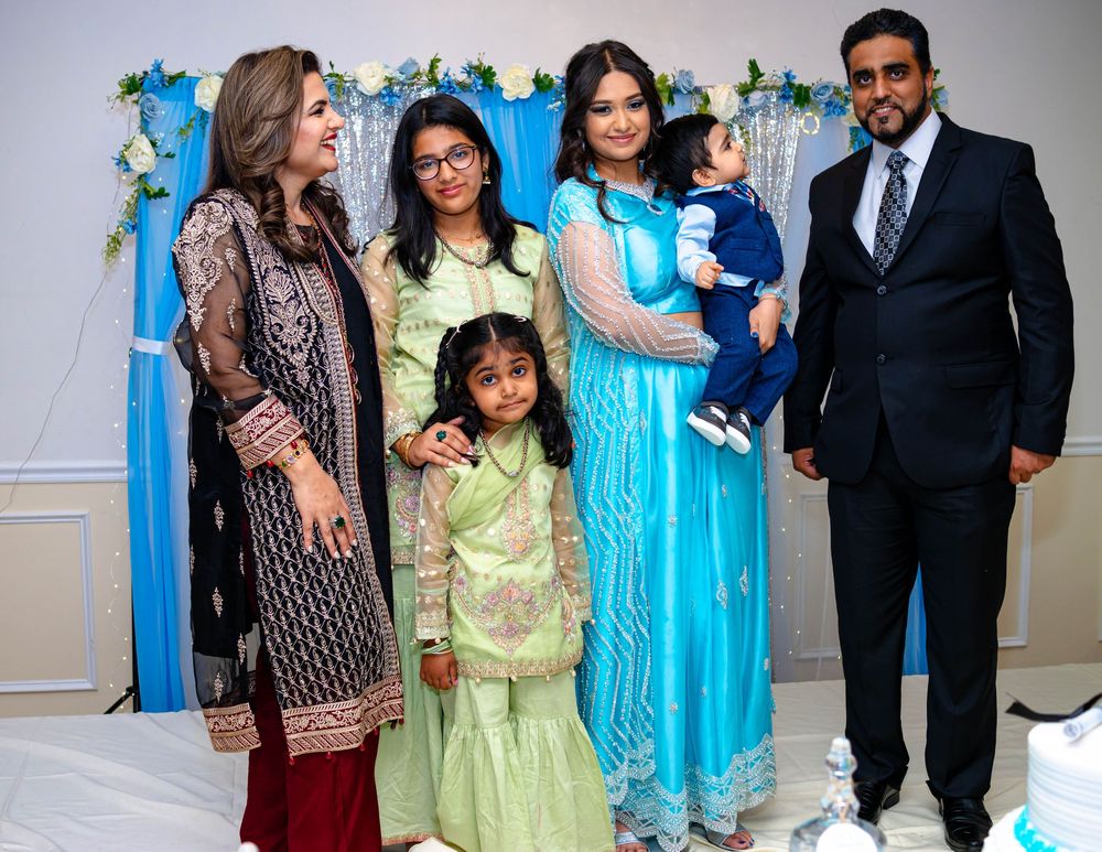 A family of five dressed in formal attire poses in front of a blue and white decorated backdrop at a celebration.