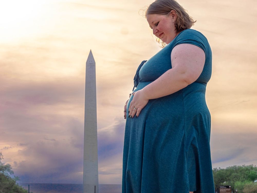 A person in a blue dress stands in front of the Washington Monument during a golden sunset.