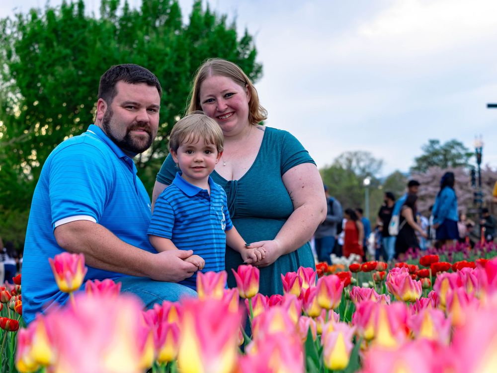 A family poses together among vibrant pink tulips blooming in a spring garden.