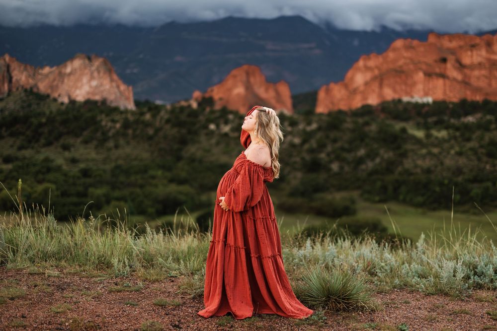 A flowing red dress stands out against the dramatic backdrop of Garden of the Gods in Colorado Springs at sunset for maternity photos.