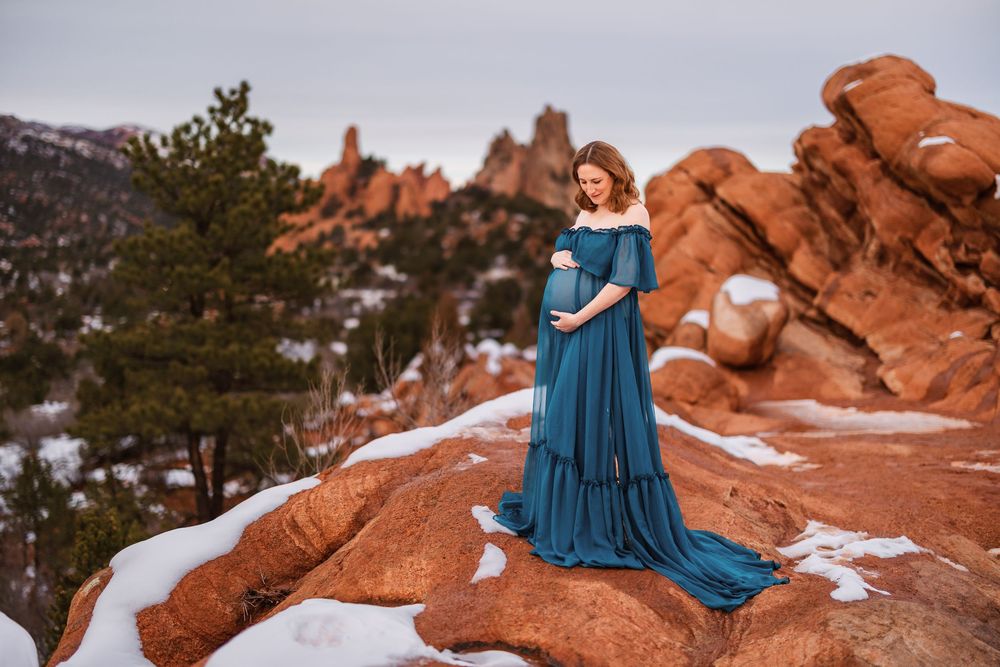 A flowing blue dress contrasts against snow-dusted red rock formations at Garden of the Gods in Colorado.