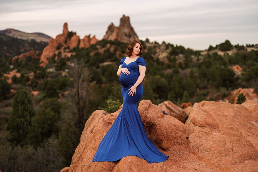 Pregnant woman in royal blue maternity gown poses on red rocks at Garden of the Gods, Colorado.