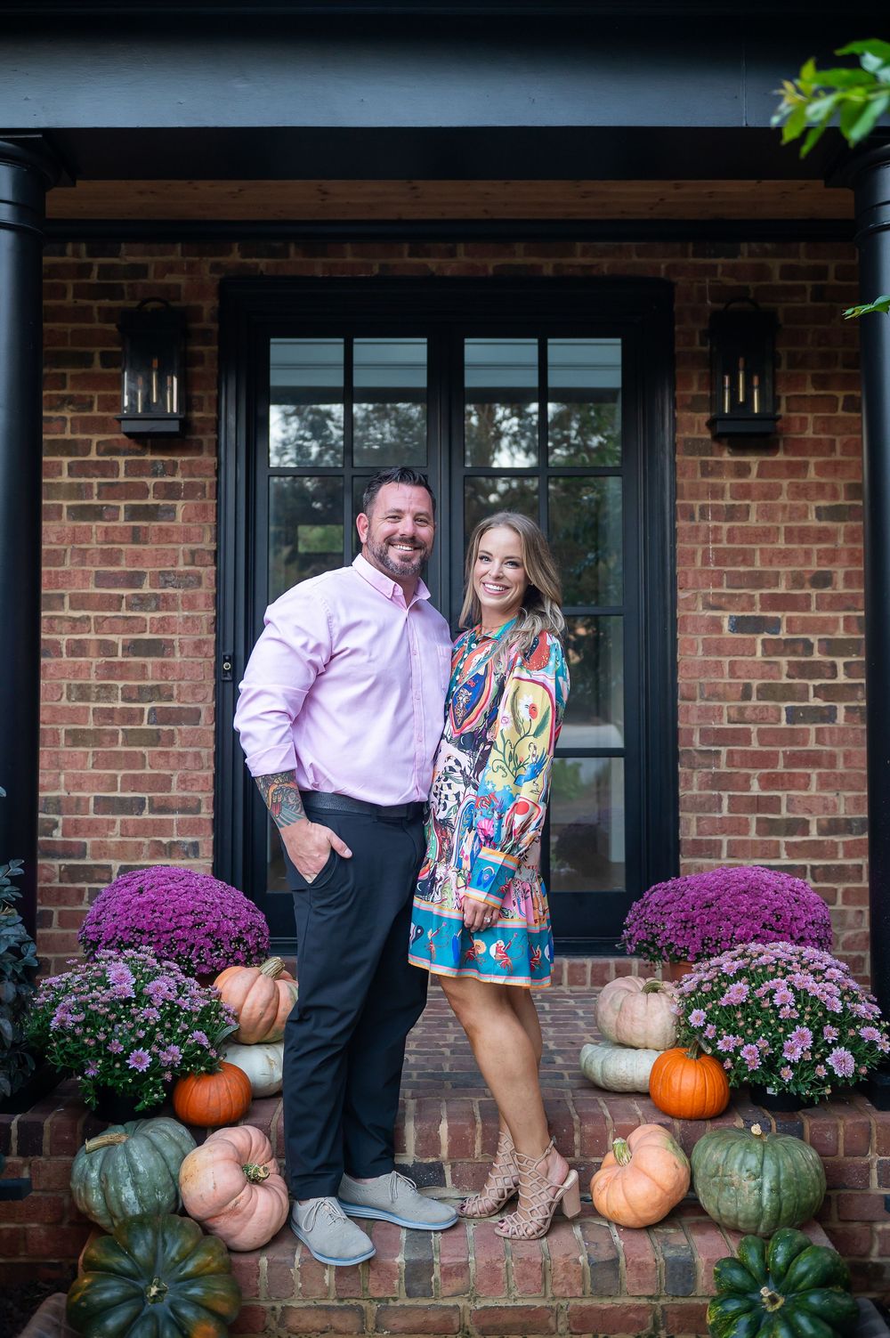 Seasonal outdoor portrait with autumn decorations including pumpkins and mums on brick porch.