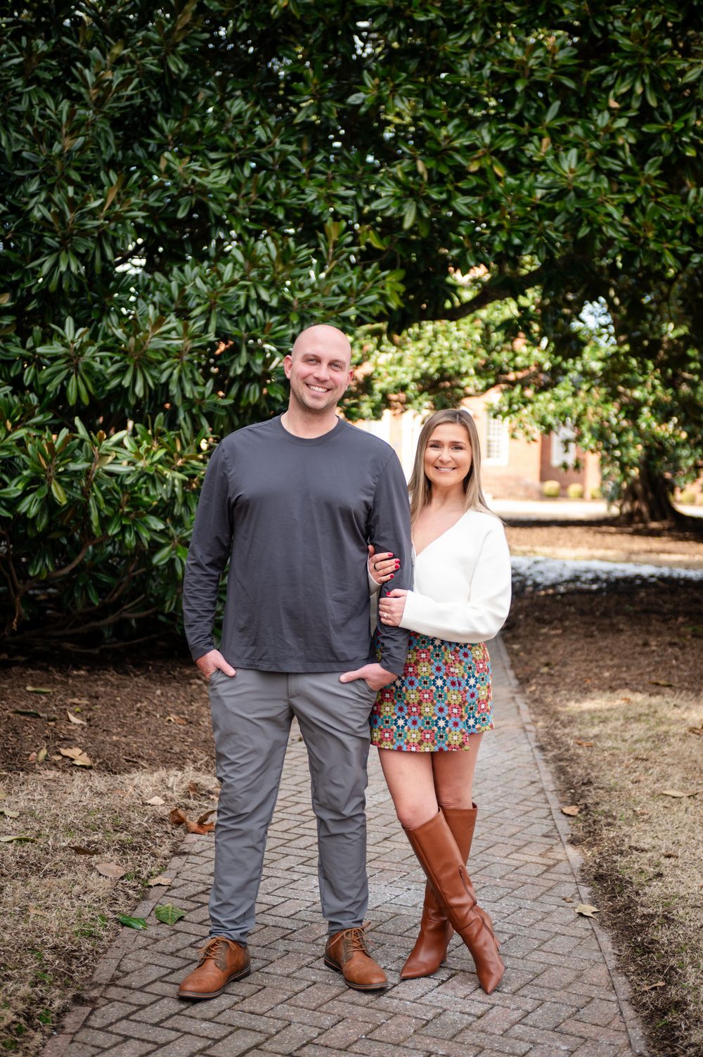 Stylish couple posing on brick pathway surrounded by magnolia trees.