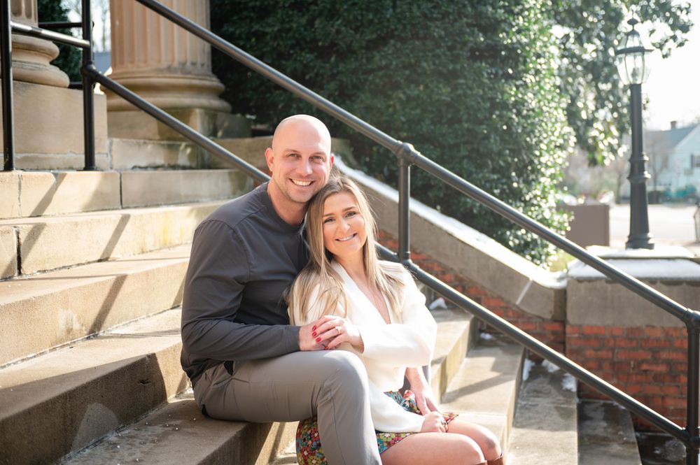 Couple embraces while sitting on outdoor stone stairs in sunny setting.