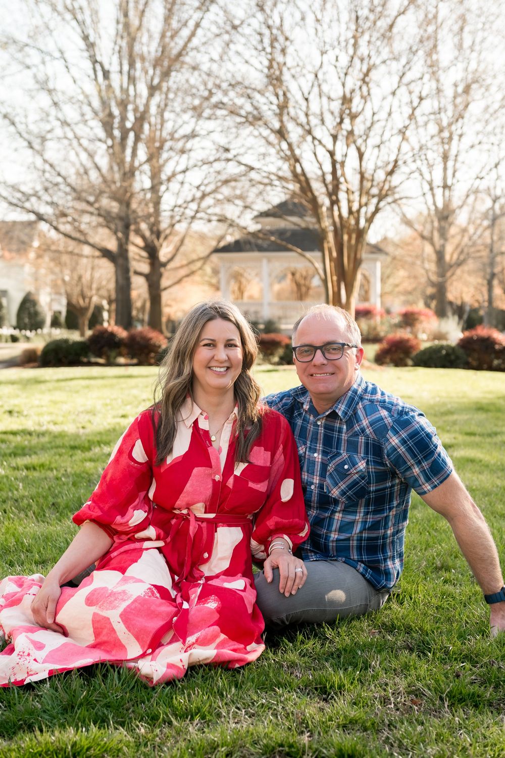 Spring engagement photos on grass with blooming trees in background.