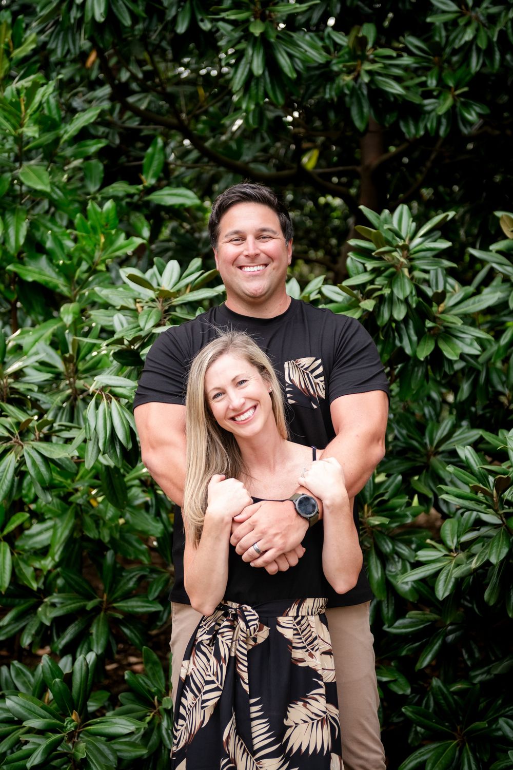 Couple embracing against lush green foliage backdrop in outdoor portrait session.