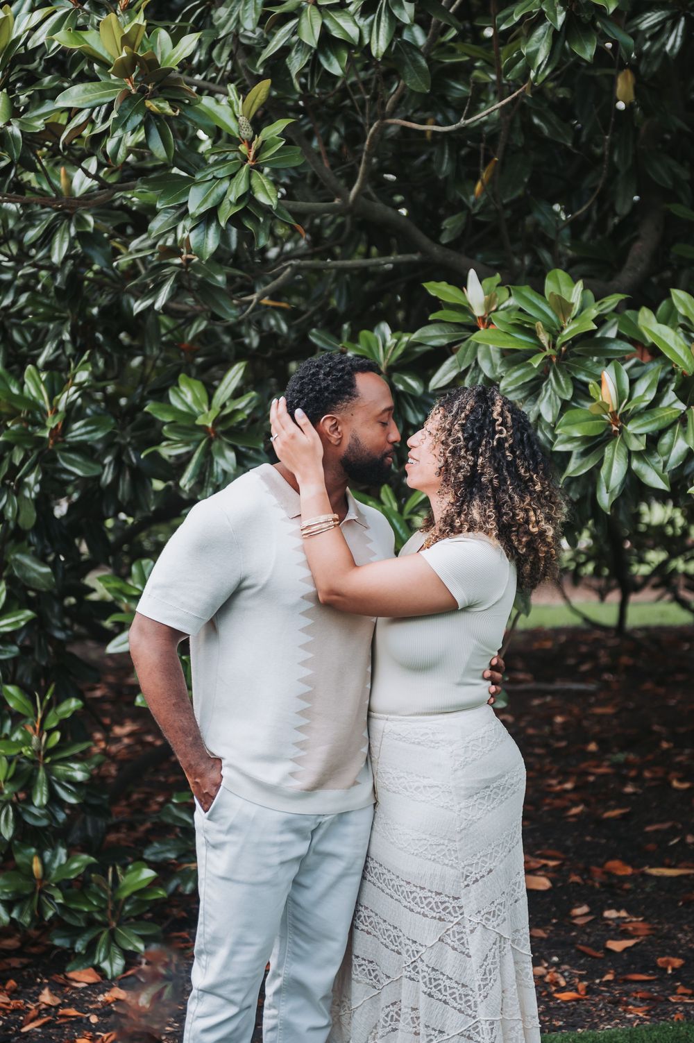 Couple in white outfits sharing intimate moments against a backdrop of magnolia trees.