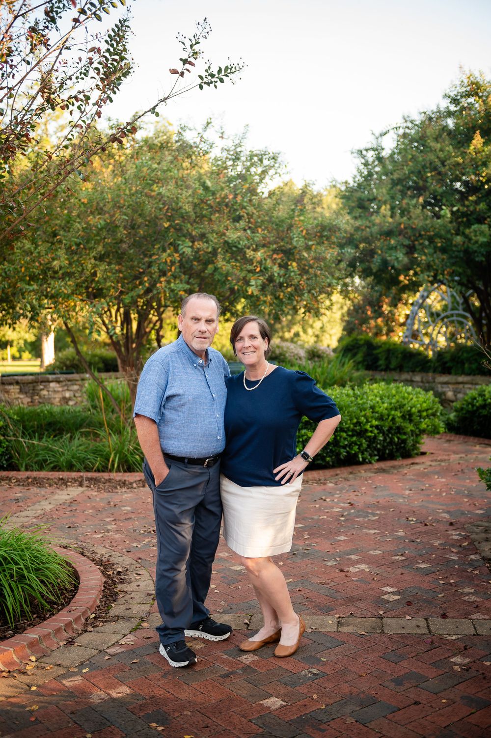 Couple posing on a curved brick path in a garden setting during golden hour.