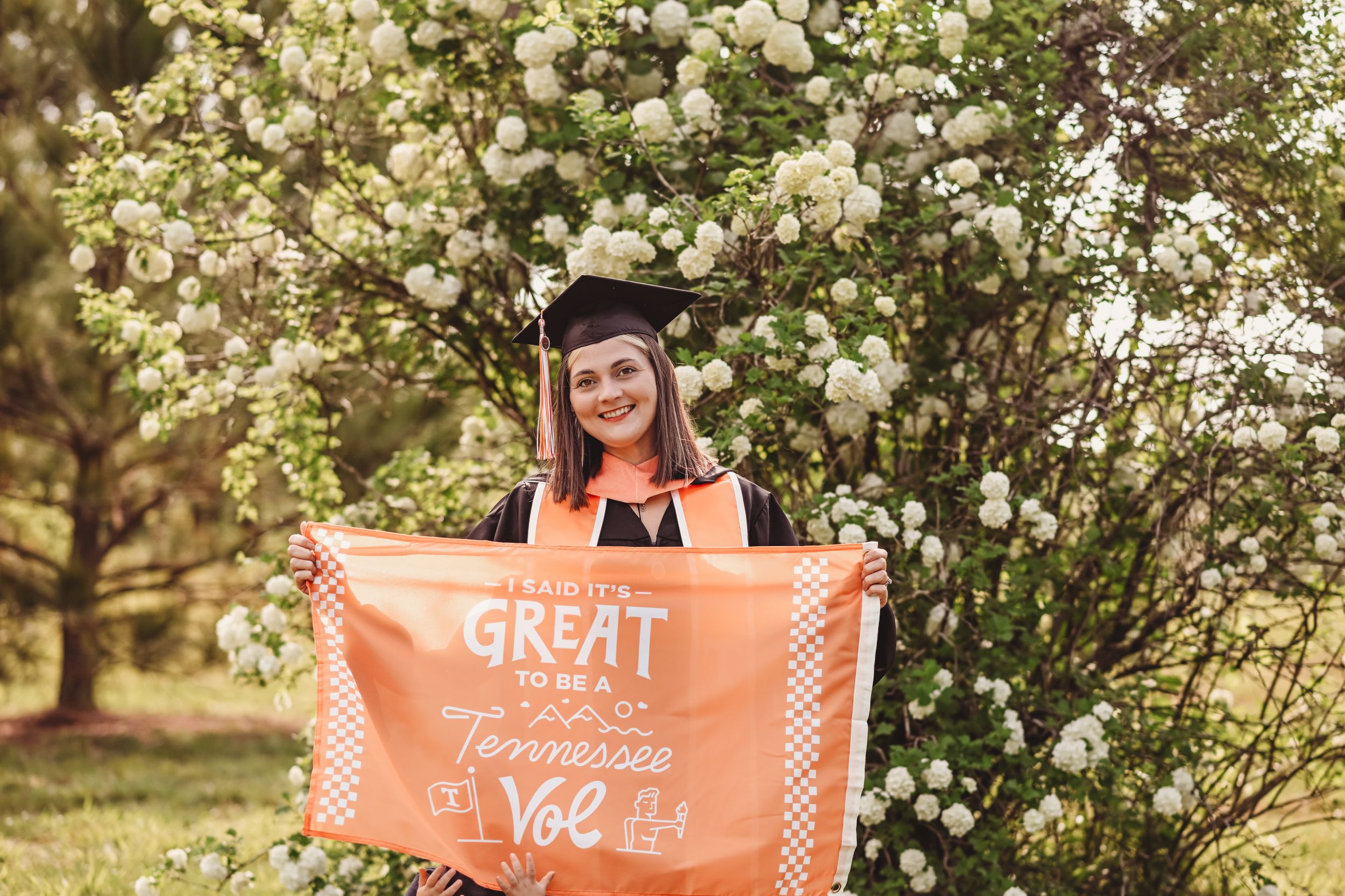 Graduation photos taken in a blooming garden with white flowers and natural lighting.