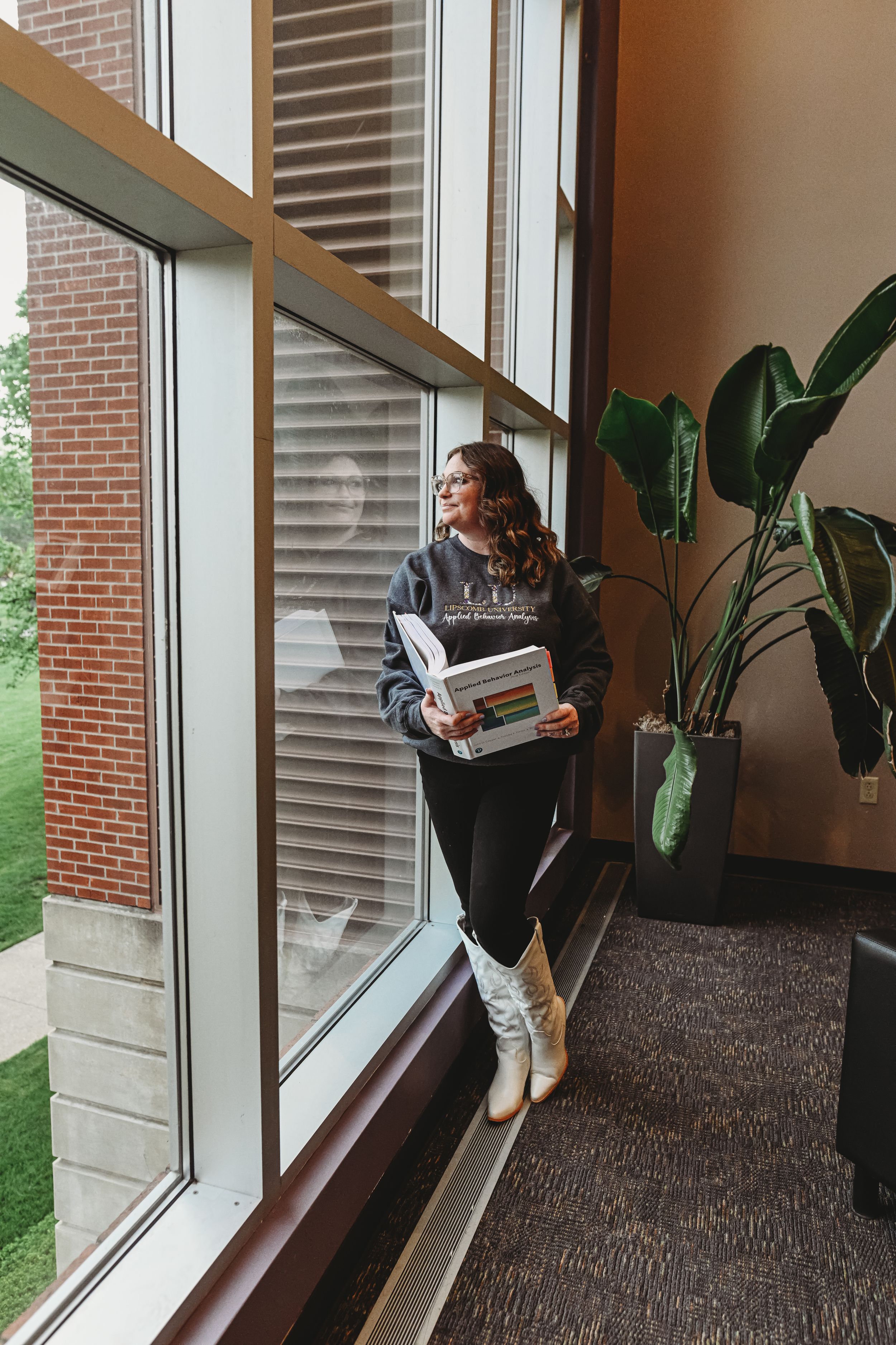Graduate poses by large windows in campus building hallway.