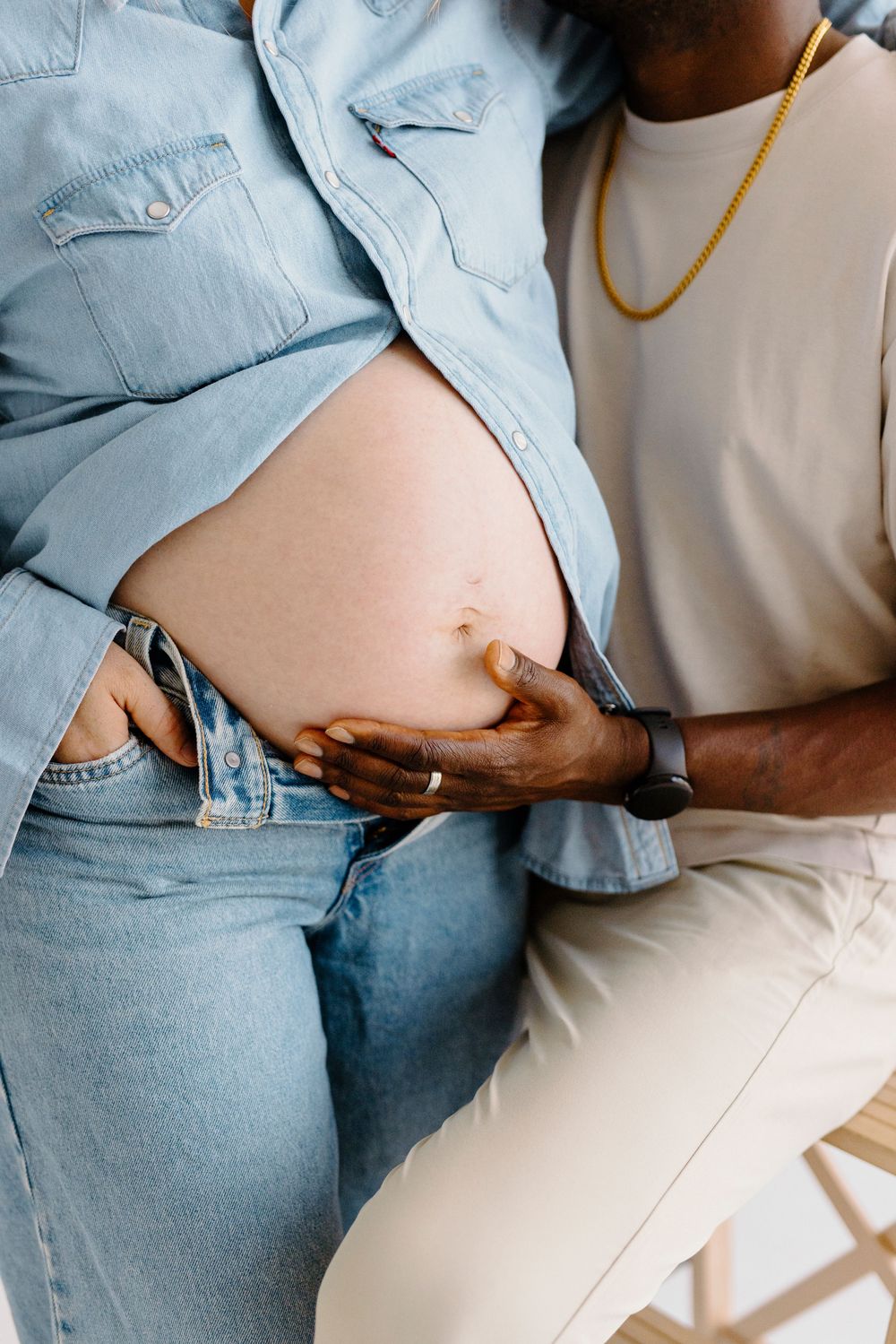 Close-up of Black man's hand gently cradling pregnant woman's bare belly during maternity photoshoot.