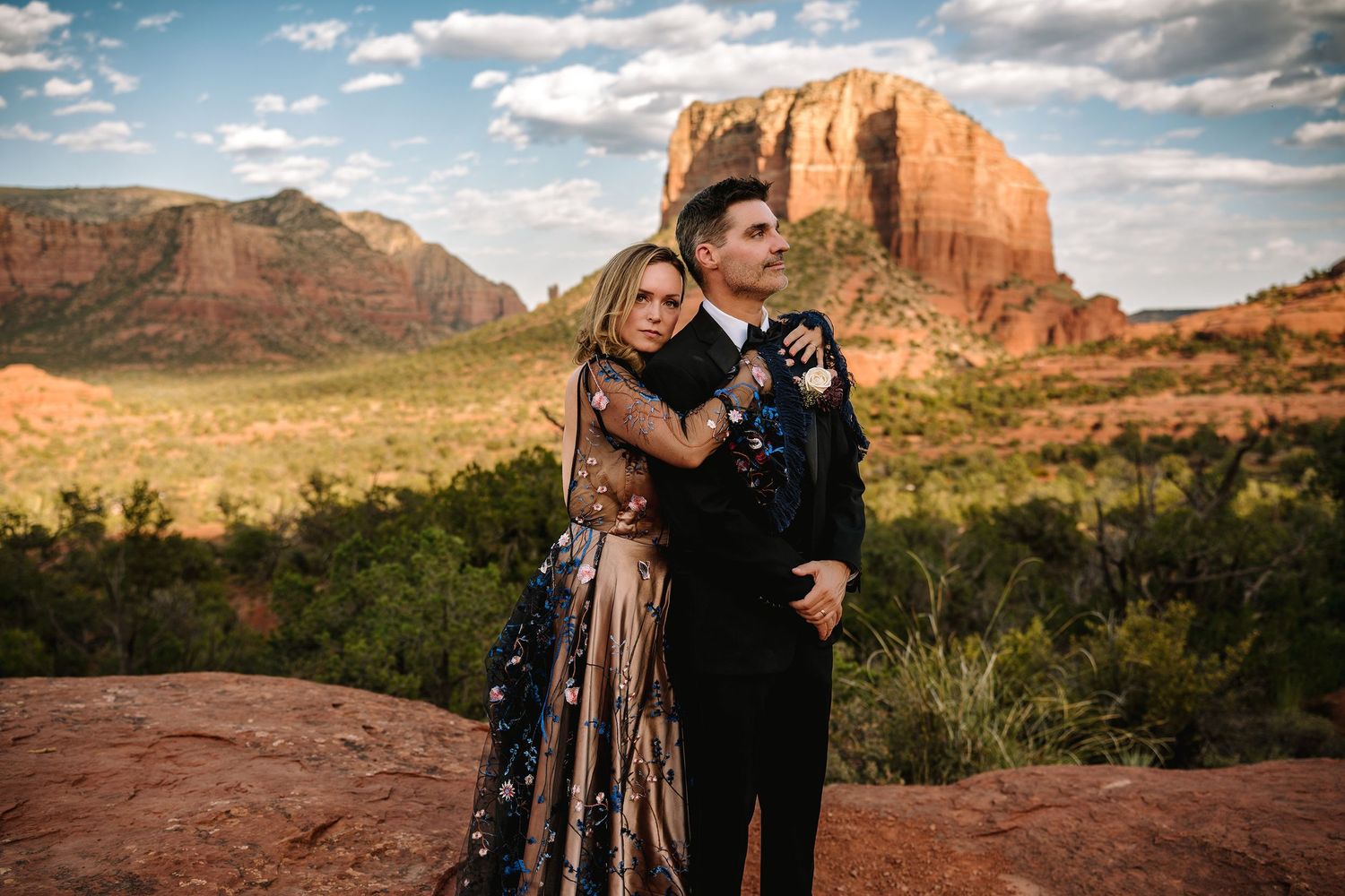Couple embracing in formal attire with stunning Sedona red rock formations and desert landscape in the background.