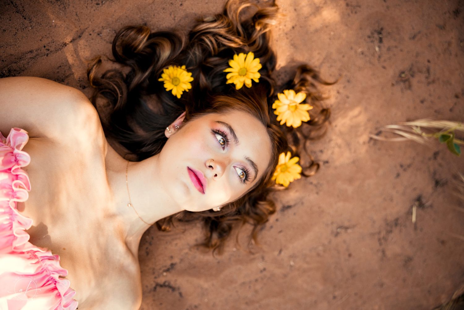 A portrait with yellow flowers in dark hair against Sedona red desert earth.